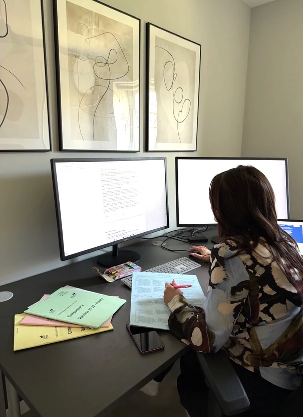 Preparing teaching materials at a desk with books and two screens